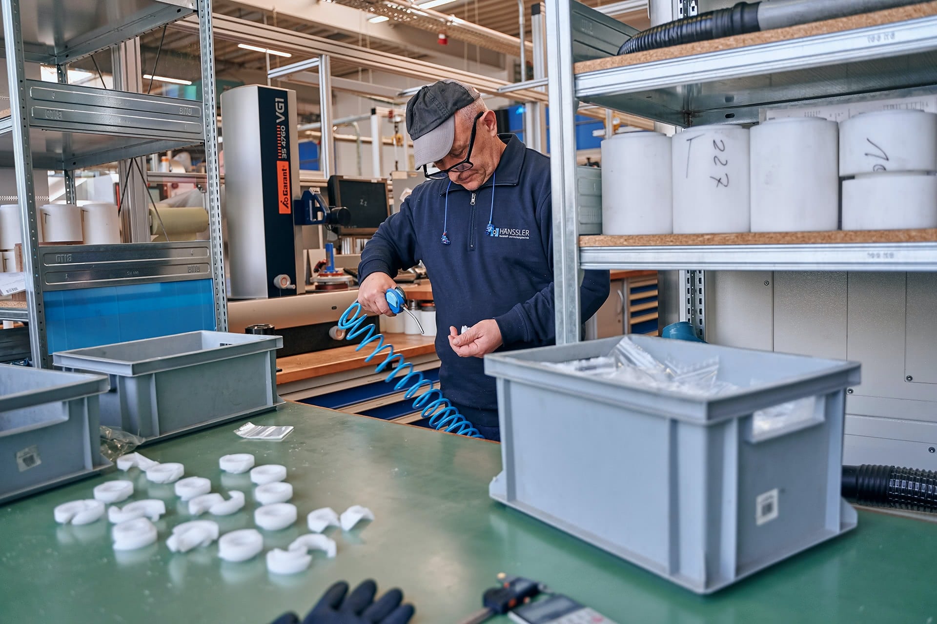 Ein Mitarbeiter säubert gefertigte Teile mit Luftdruck von Produktionsresten