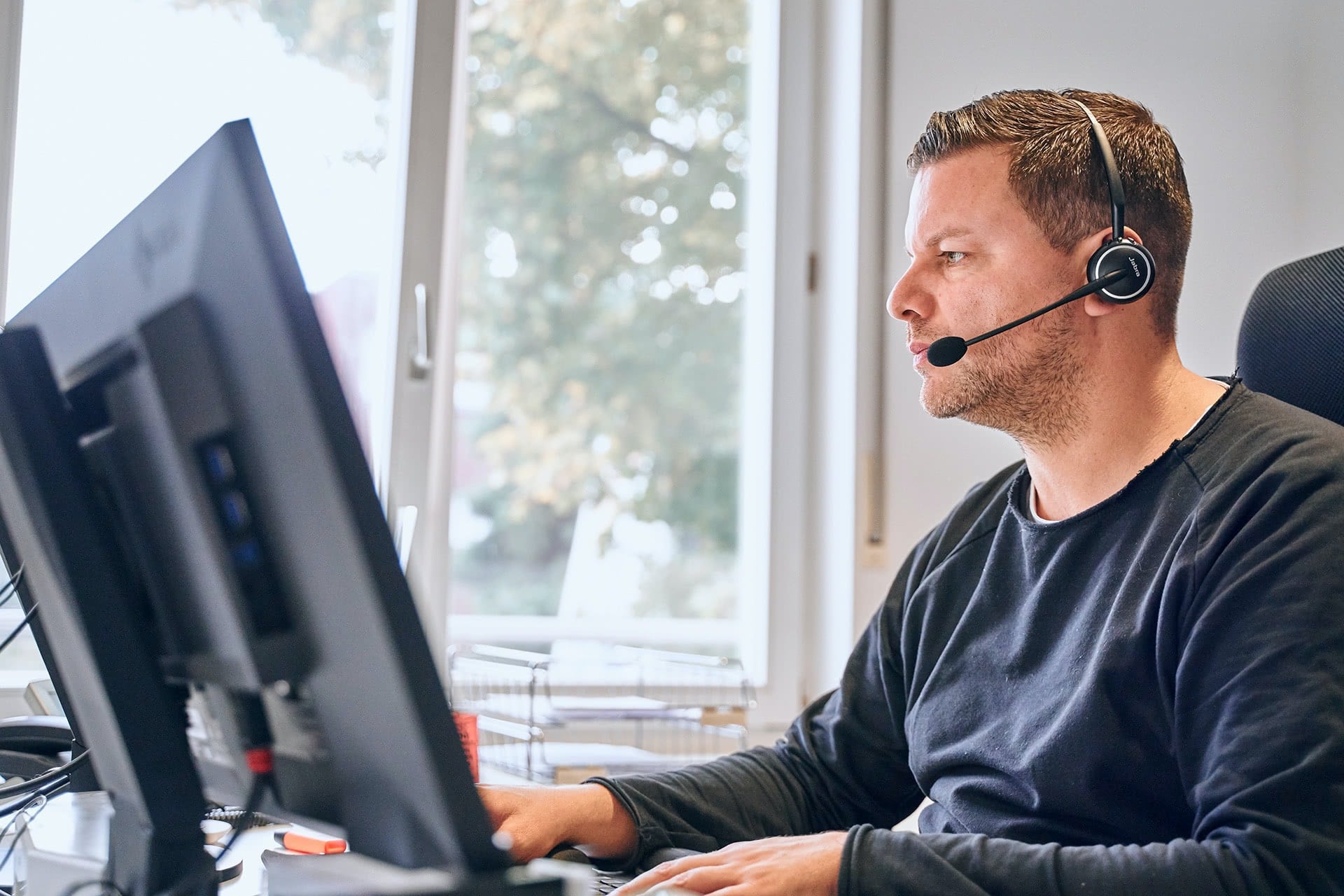 Ein Mitarbeiter arbeitet mit Headset vor dem Bildschirm