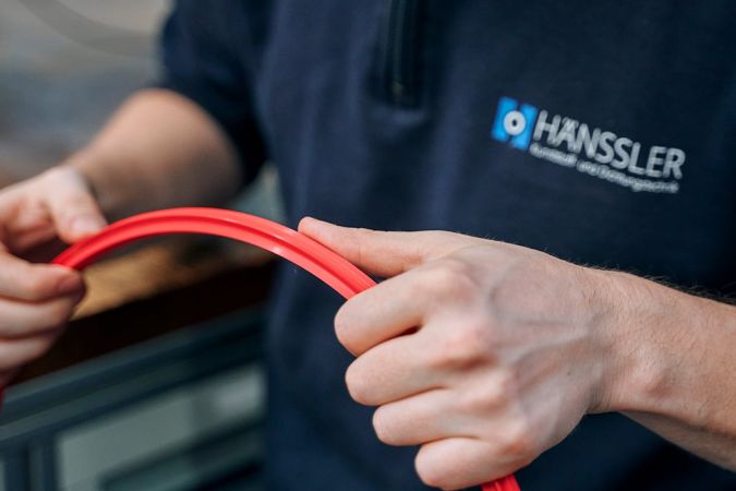 Ein Mitarbeiter, welcher eine rotes Drehteil aus Elastomer prüft