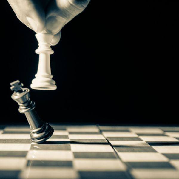 A hand knocking over a black chess piece on a chessboard with a white chess piece